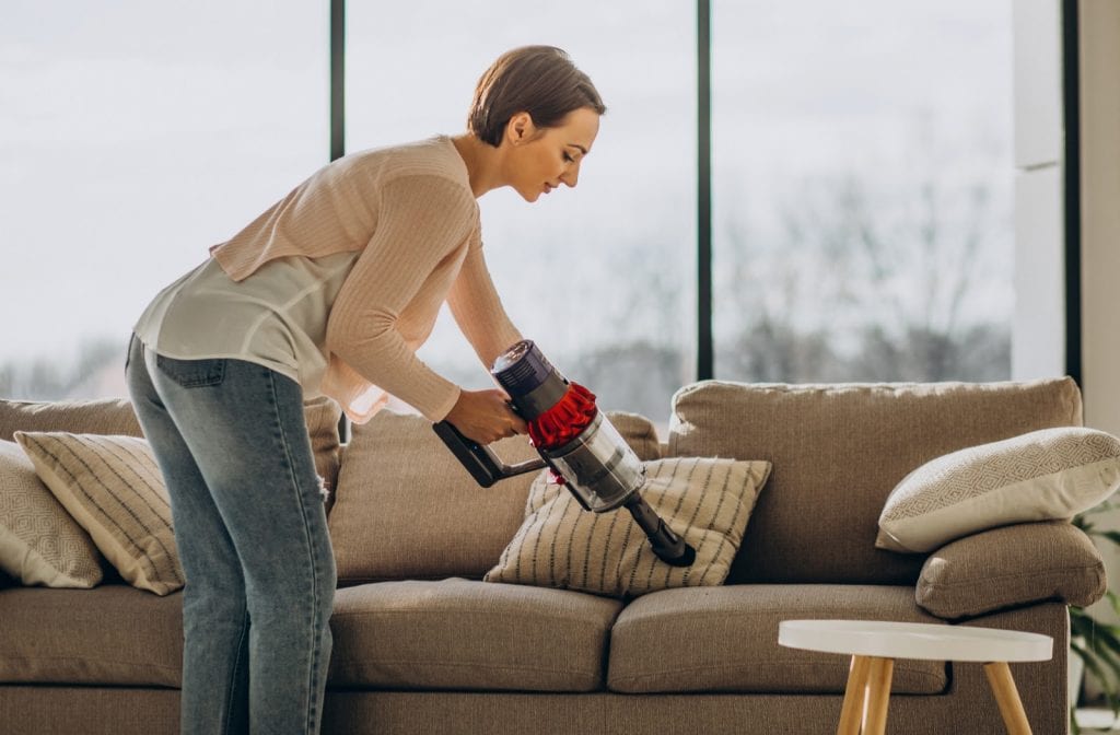 Woman cleaning her sofa with portable vacuum in her house