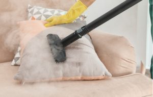 Person cleaning sofa cushion with steam cleaner