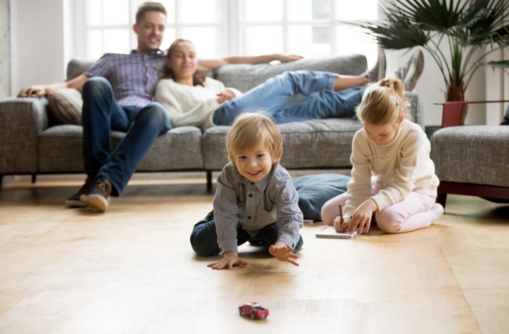 Kids playing on the ground with toys with parents sitting on couch in living room
