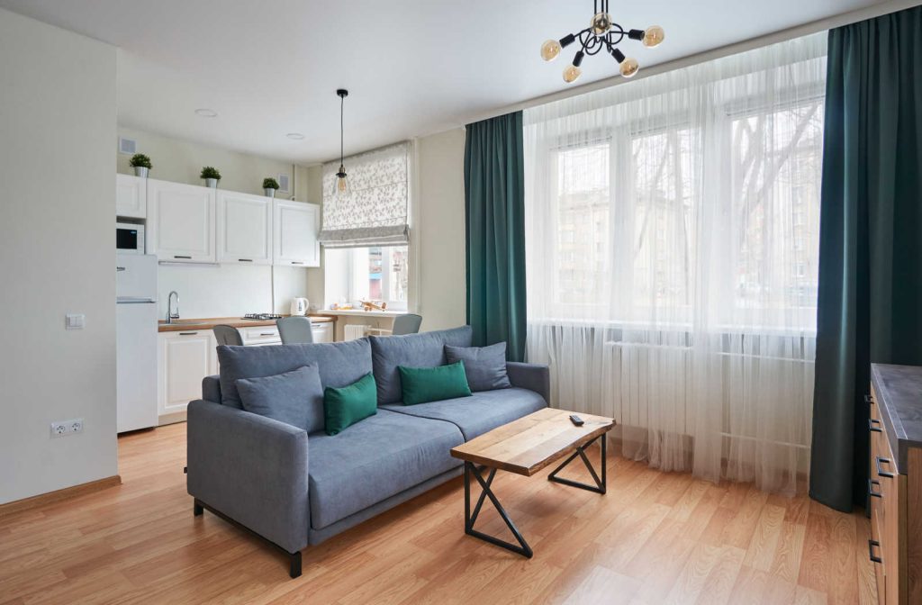 A grey sofa and wood coffee table sit in the middle of a living room separating the kitchen space.