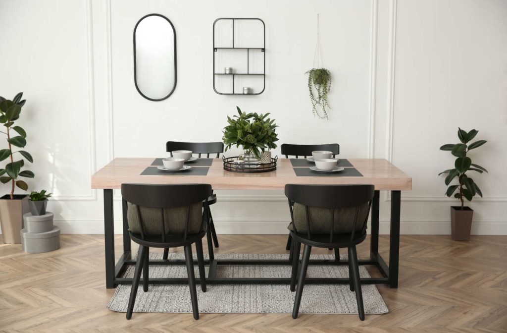 Wooden dining table with black wooden chairs, white bowls placed on the table and a decorative plant in the middle.