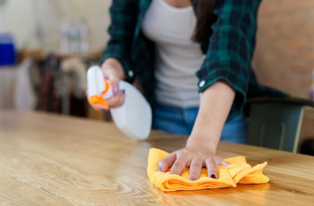 A woman using cleaning fluid and a cloth to clean her solid wood dining table.