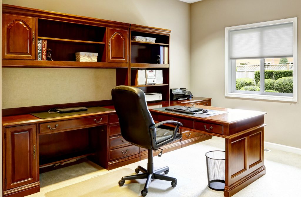 An L-shaped wooden desk with shelves and drawers for storage and a window allowing natural light to fail straight on the desk.
