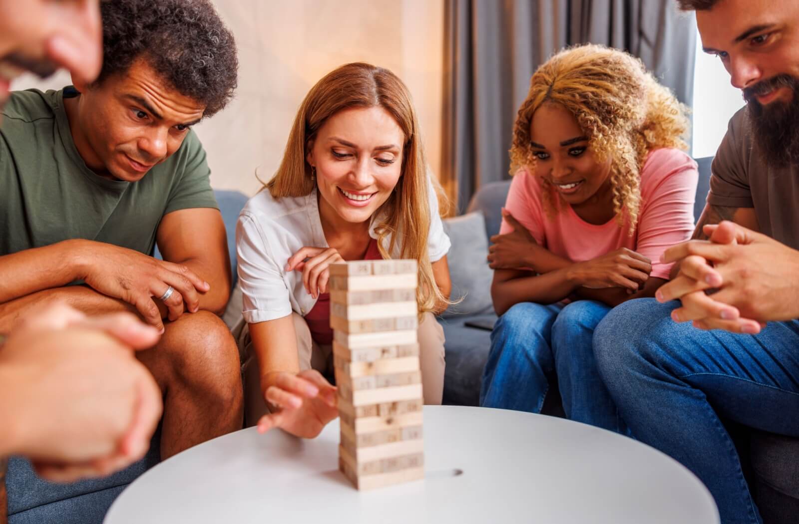 A group of people playing Jenga while sitting around a coffee table.