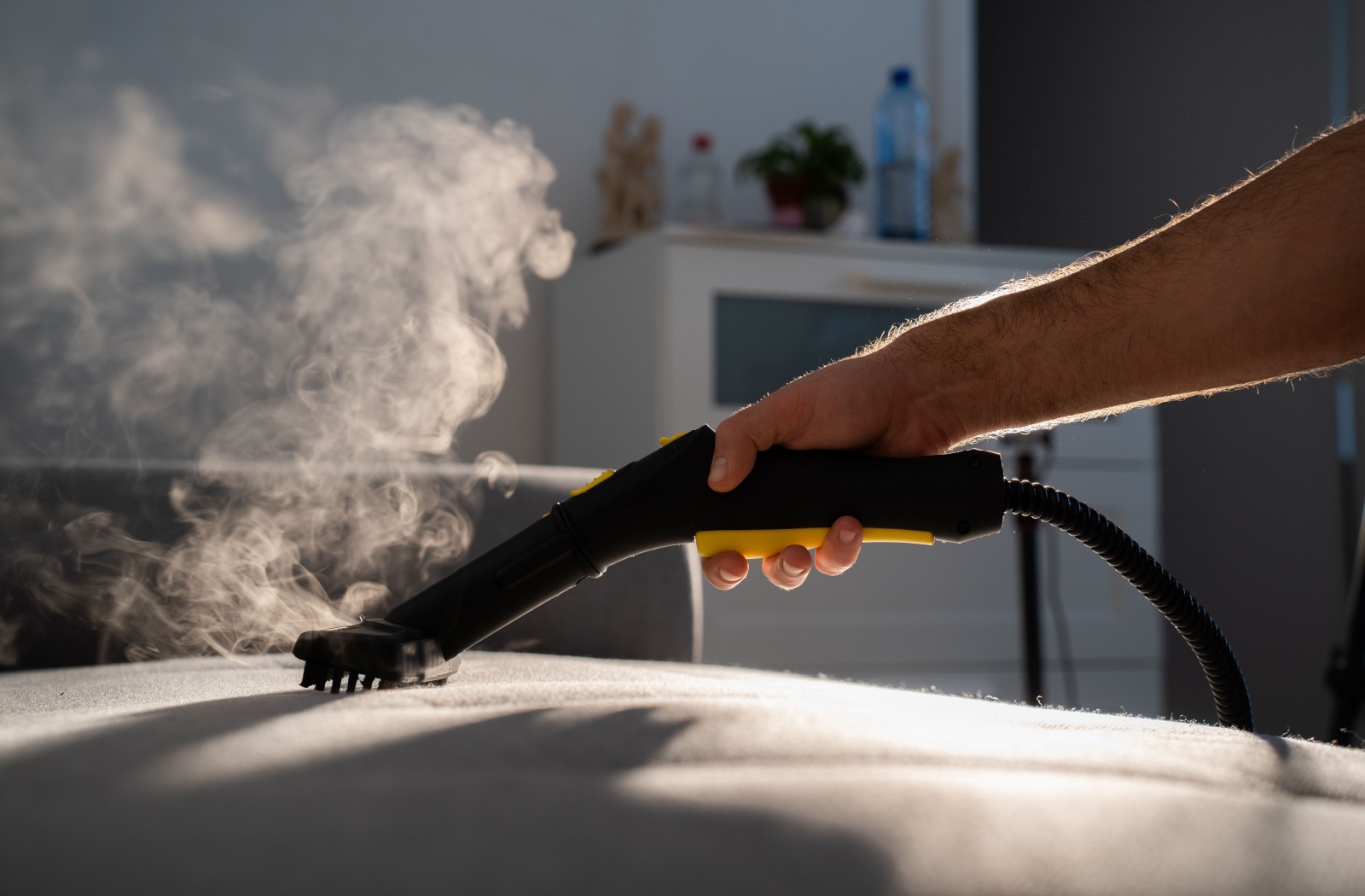 Steam coming from a steam cleaner as someone uses it to deep clean an upholstered fabric couch.