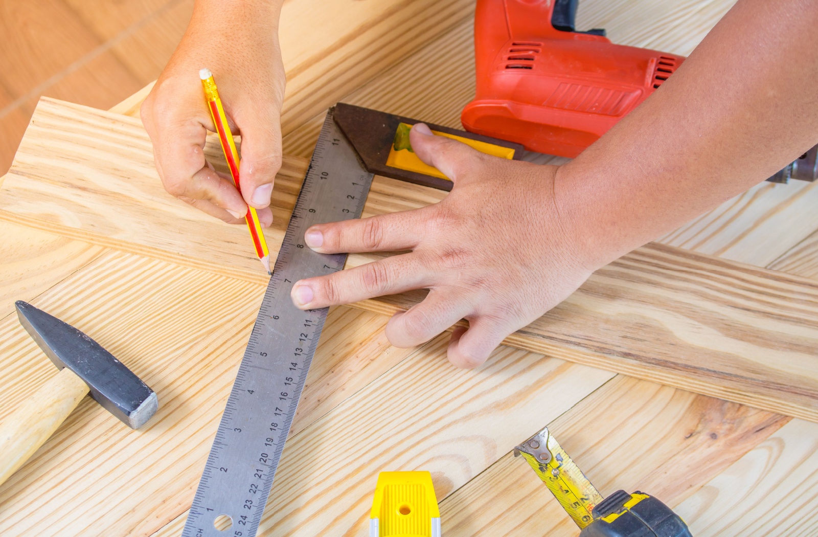 A carpenter using a pencil and ruler to measure a piece of wood while making solid wood furniture.