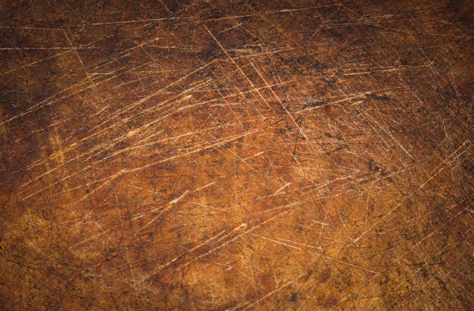 A close-up image of the surface of a wood table covered in scratch marks.