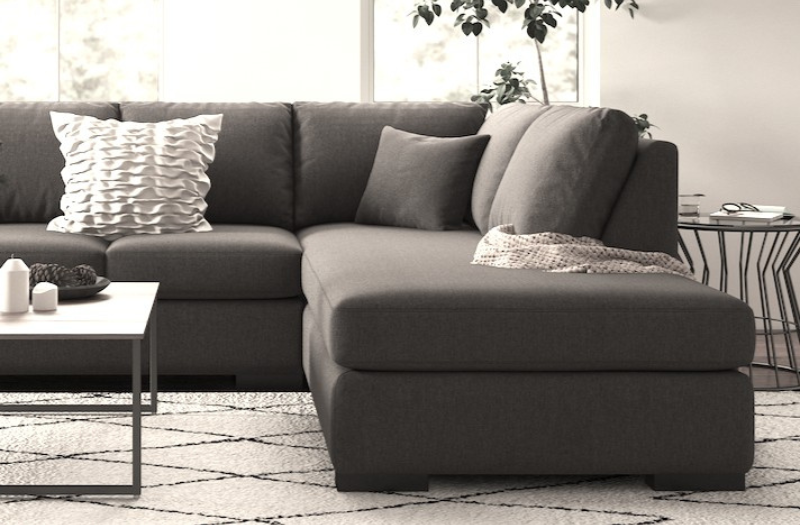 Grey sofa with a blanket, a pillow, a wooden coffee table and a plant on a wooden floor in a minimalist interior